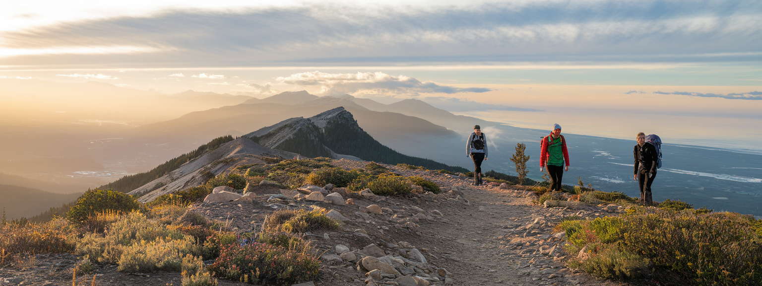 Hiker on an alpine ridge overlooking Whistler Mountain Trails with snow-capped peaks and blue sky